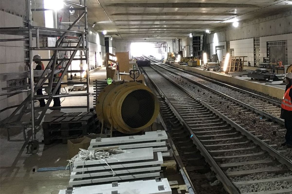 Ein Bauarbeiter steht auf einer Bahngleisanlage in einem Tunnel, umgeben von Baustellenmaterial und Werkzeug.