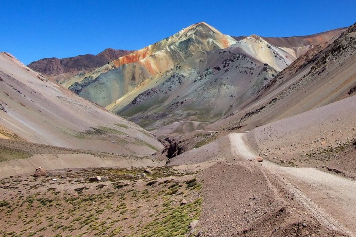 Eine faszinierende Berglandschaft mit farbenfrohen Felsen und einer kurvigen Schotterstraße in einer trockenen Umgebung.