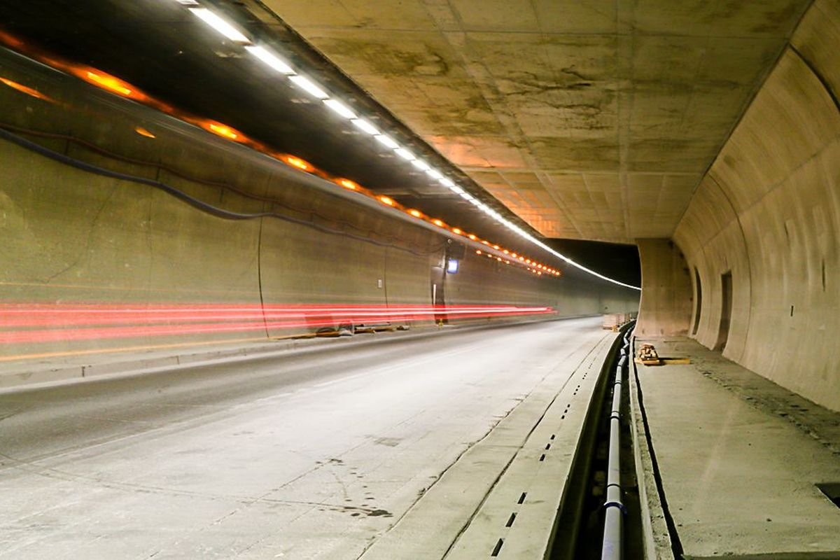 Ein Tunnel mit Betonwänden, beleuchtet von Deckenleuchten, lässt Autofahrten sichtbar werden. Rechts sind Öffnungen in der Wand.
