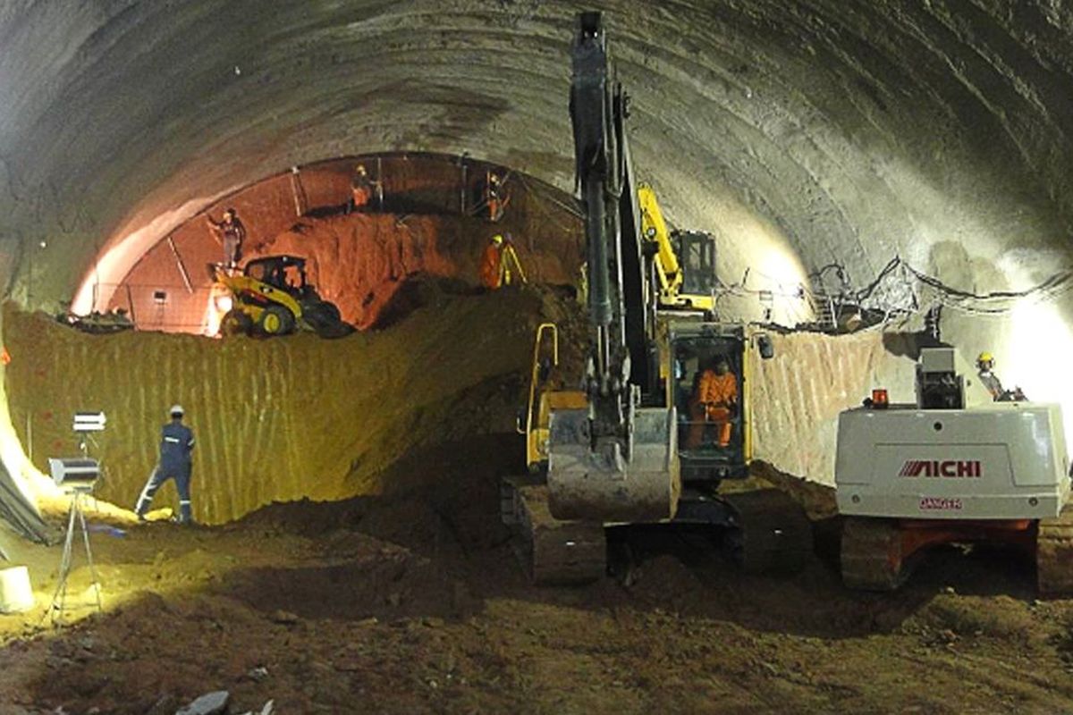 Bauarbeiten in einem Tunnel mit Baumaschinen und Arbeiter*innen, beleuchtet von Scheinwerfern.