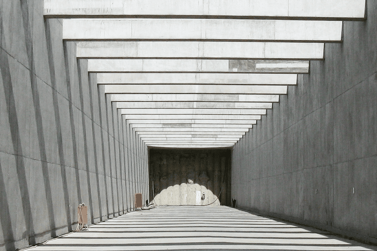 Ein langer, grauer Tunnel mit einem klaren Licht am Ende, flankiert von Betonwänden und orangefarbenen Elementen.