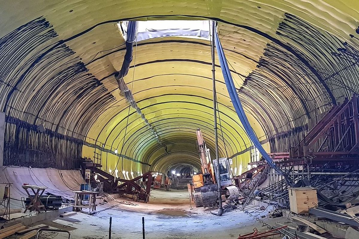 Eine Baustelle in einem Tunnel mit gelb gestrichener Decke und verschiedenen Baugeräten und -materialien.
