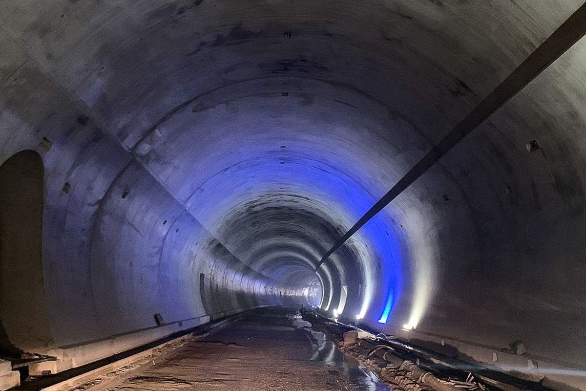 Ein langer, beleuchteter Tunnel mit geraden Wänden und Schienen am Boden, der in die Dunkelheit führt.
