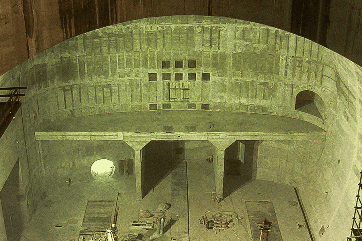 Eine große, unvollendete, betonierte Baugrube mit einem geschwungenen Dach und Baugerüsten im Hintergrund.