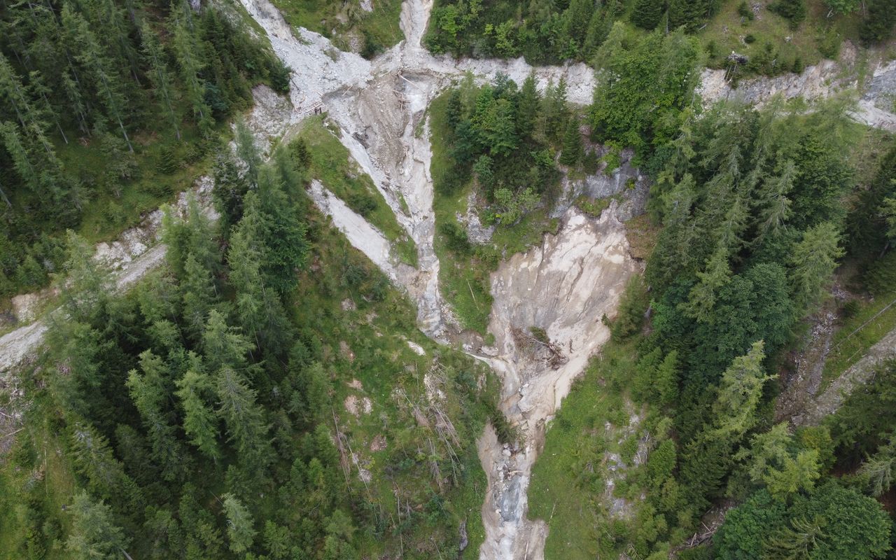 Luftaufnahme einer bewaldeten Landschaft mit einem erodierten Bereich und einem Flussbett, von Bäumen umgeben.