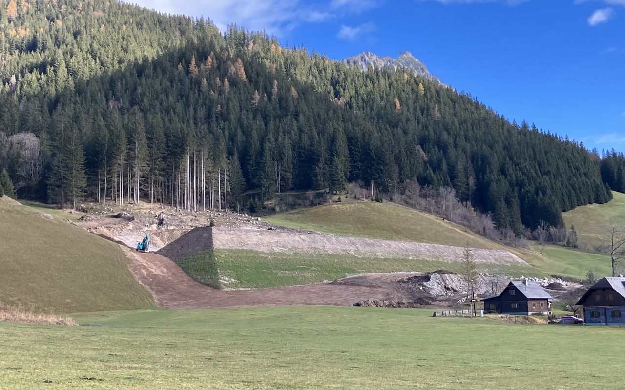 Eine Baustelle in einer grünen Landschaft mit Bäumen und Bergen im Hintergrund, Nebel und blauer Himmel.