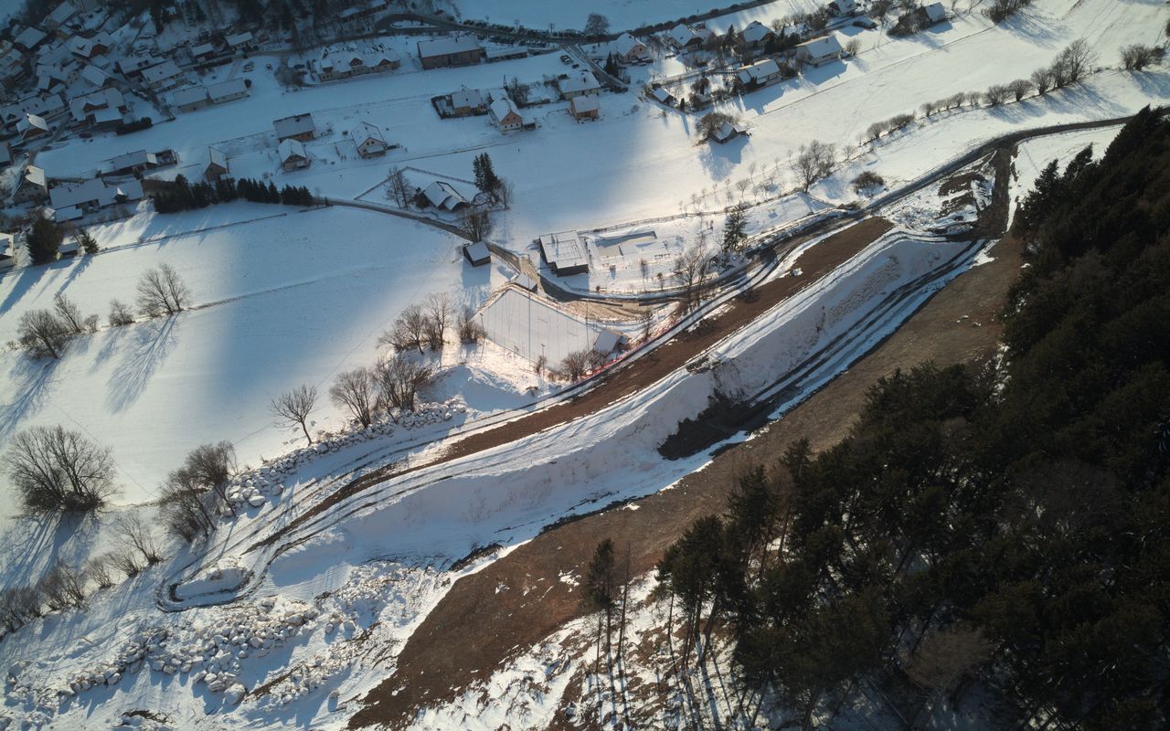 Luftaufnahme einer schneebedeckten Landschaft mit Dörfern, Bäumen und einer geschwungenen Straße im Vordergrund.