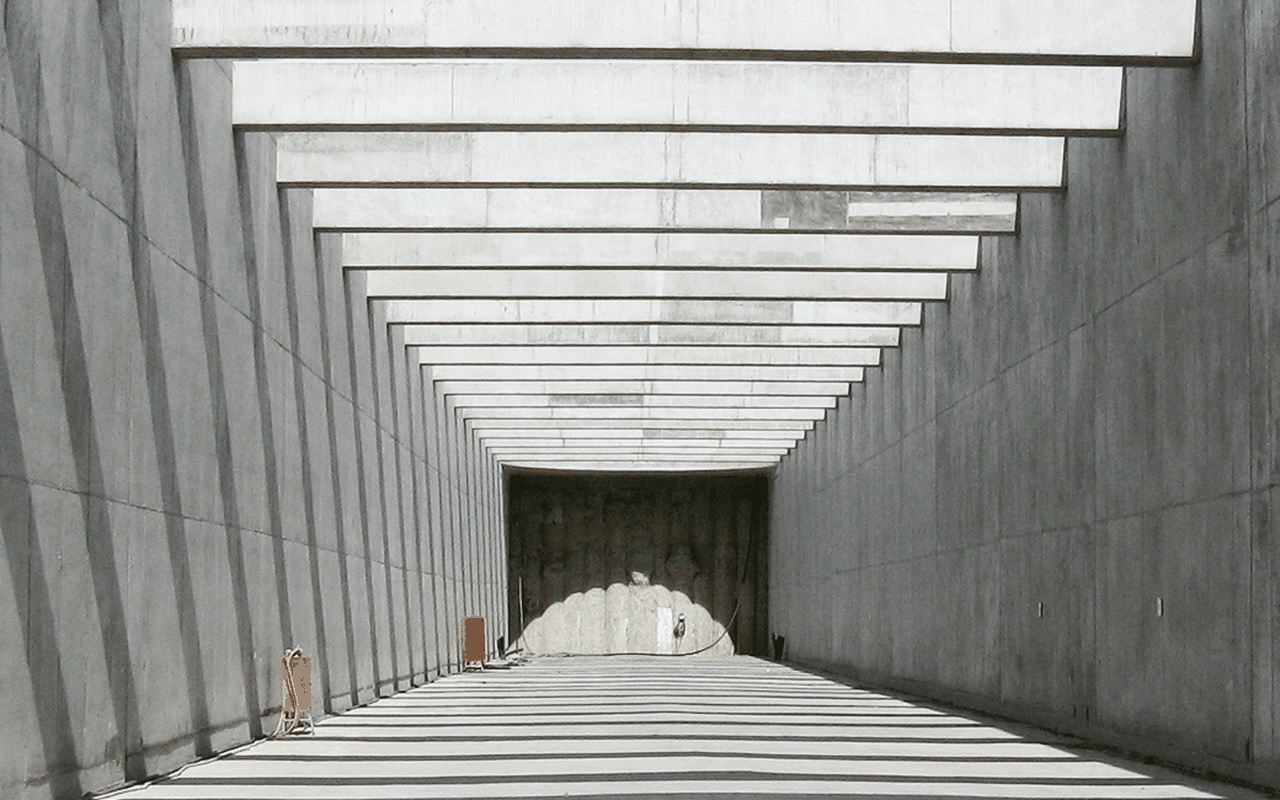 Ein langer, grauer Tunnel mit einem klaren Licht am Ende, flankiert von Betonwänden und orangefarbenen Elementen.