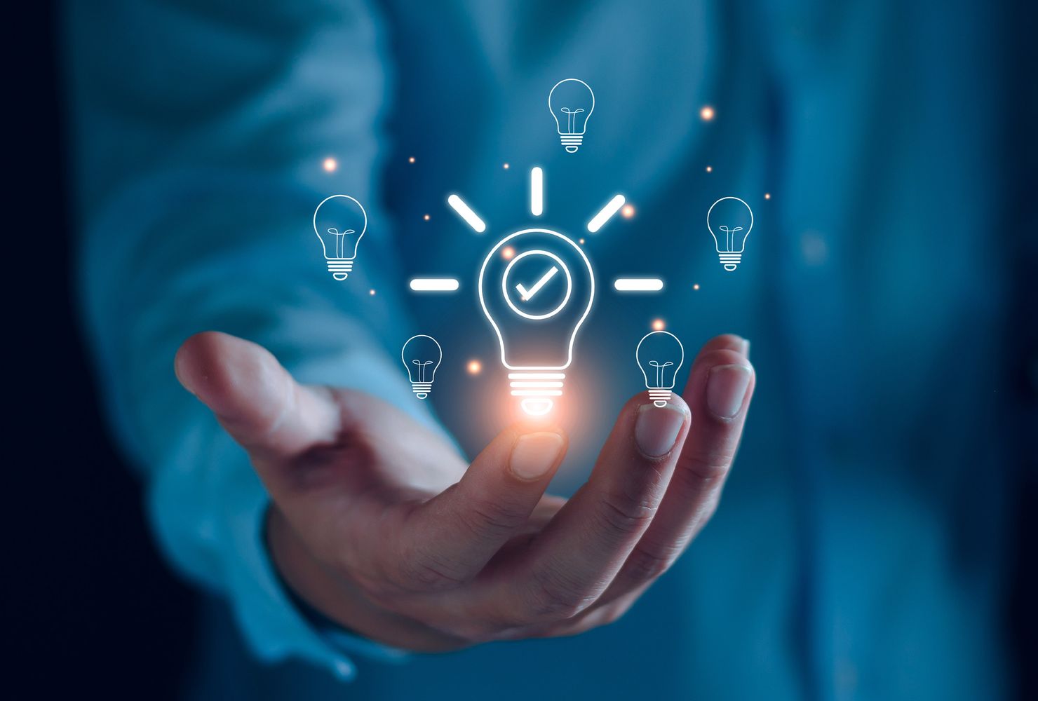 Eine Hand hält eine glühende Glühbirne umgeben von kleinen, leuchtenden Glühbirnen und funkelnden Effekten.