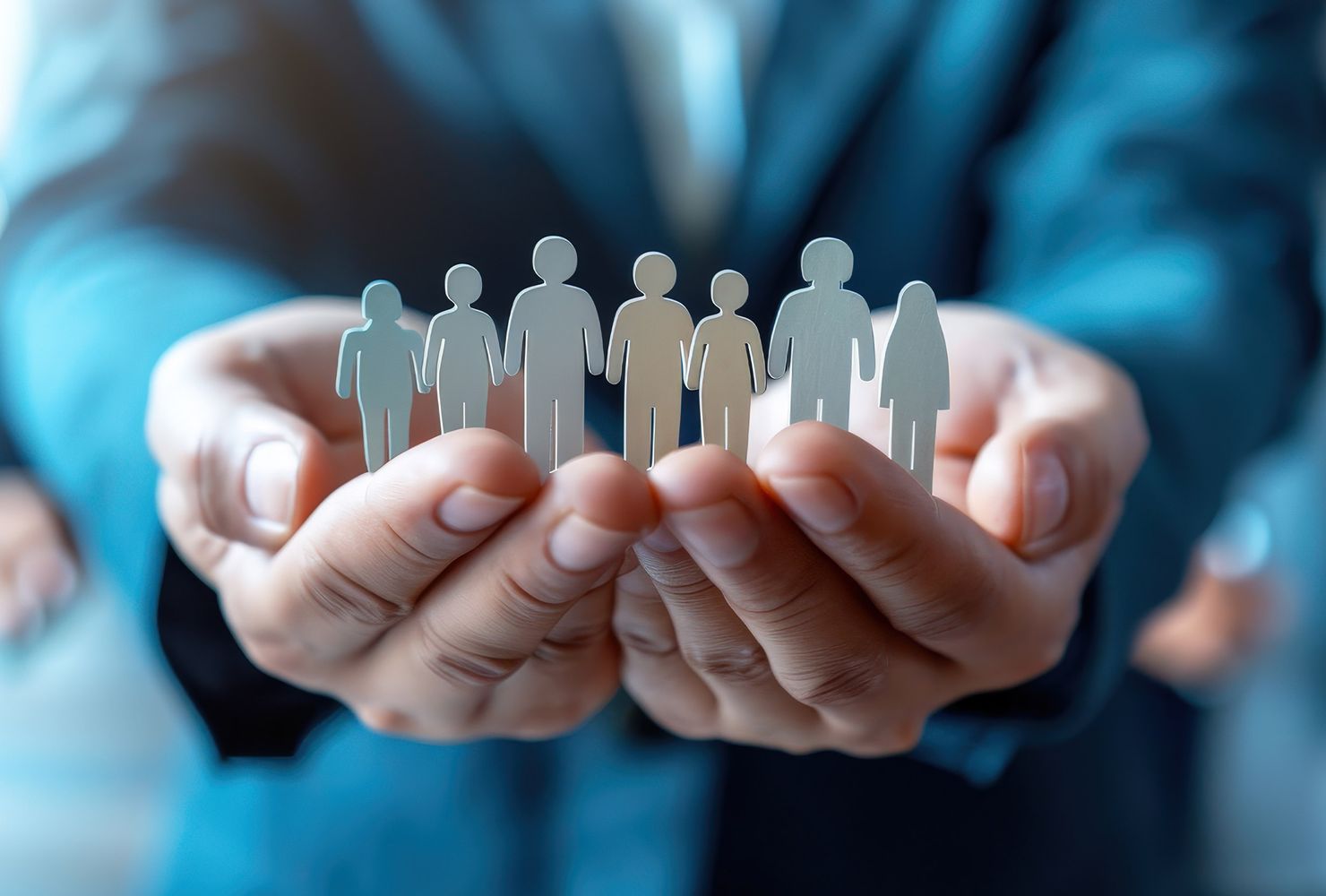 Zwei Hände halten Figuren von Menschen in verschiedenen Größen, symbolisierend Gemeinschaft und Zusammenarbeit.