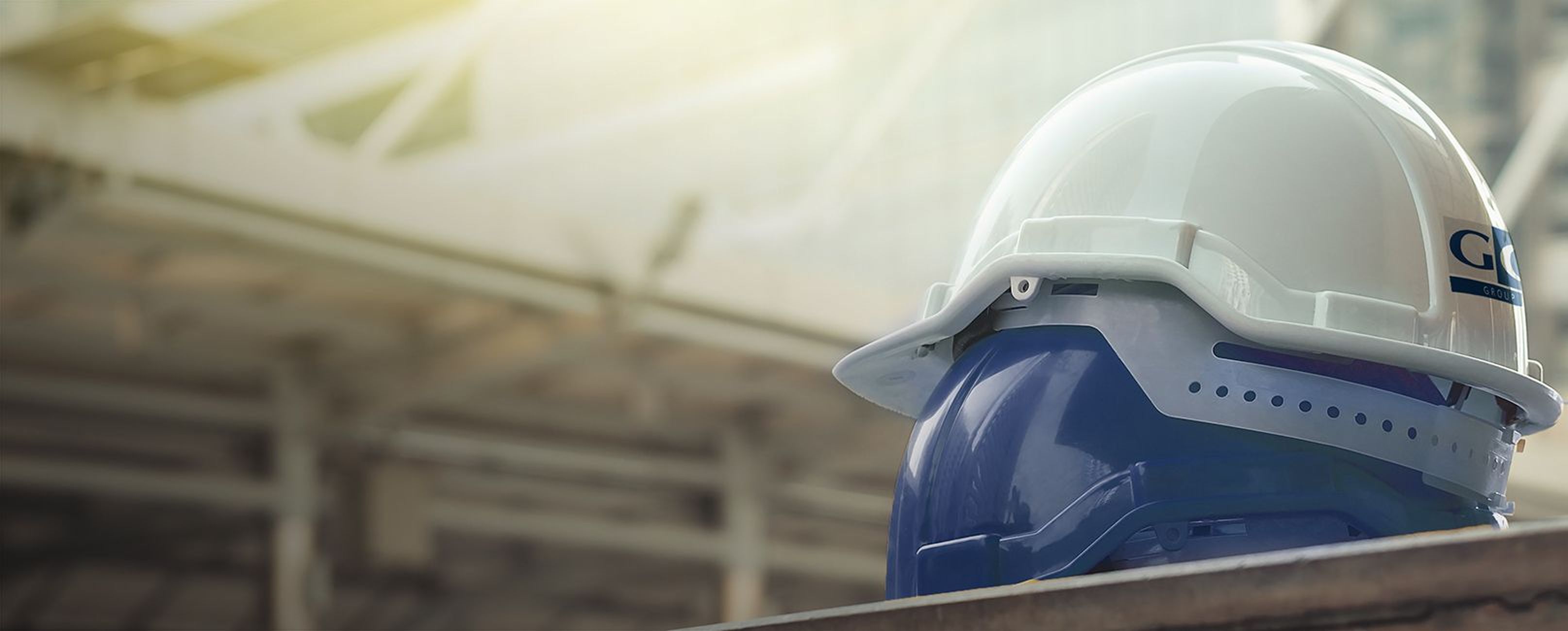 Ein weißer Schutzhelm und ein blauer Gesichtsschutz, der auf einer Metalloberfläche mit einem unscharfen industriellen Hintergrund ruht.