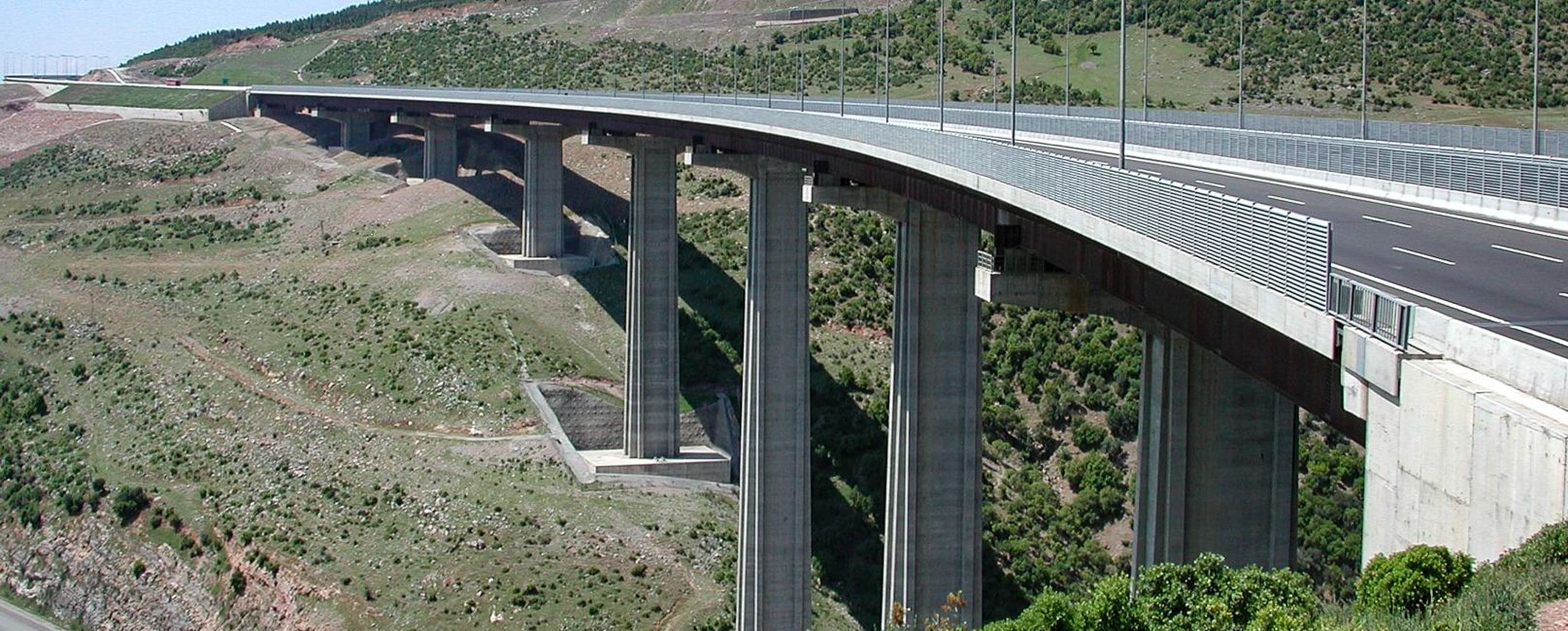 Eine hochgelegene Brücke über ein hügeliges Terrain mit grünen Böden und einer asphaltierten Fahrbahn.