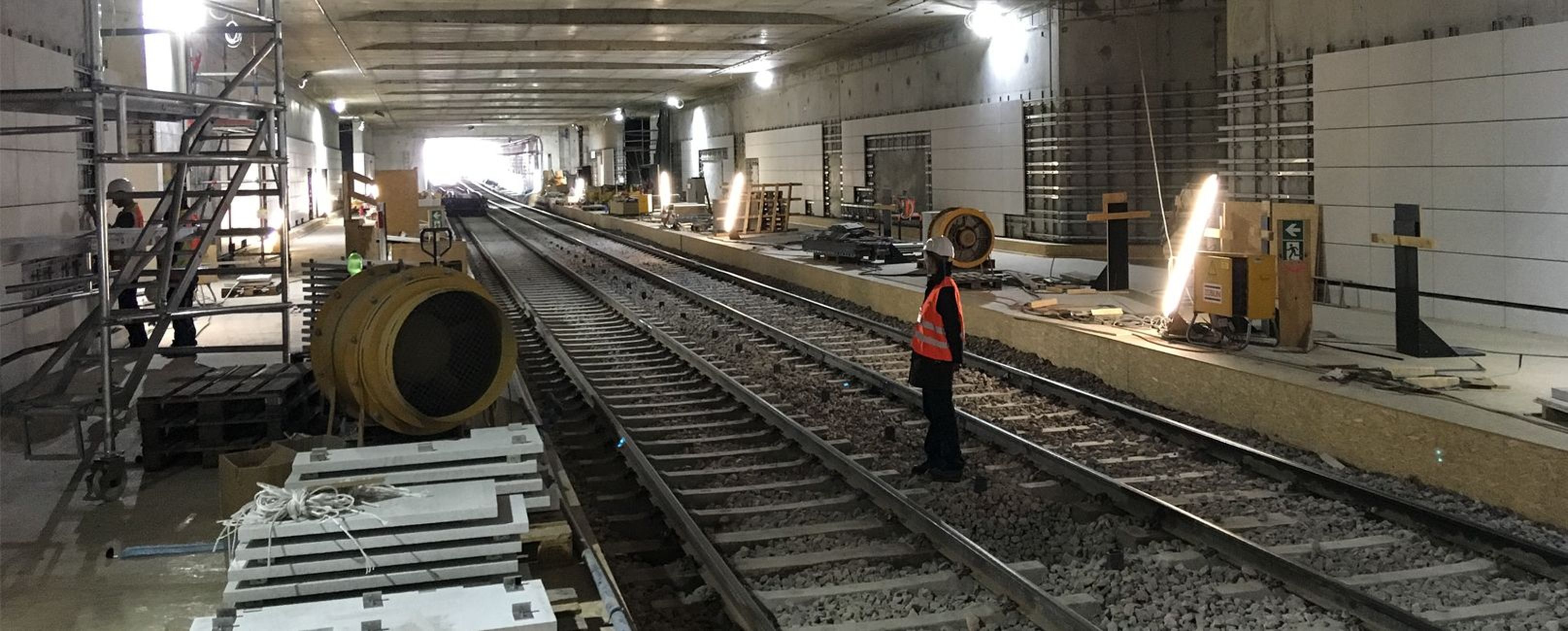 Ein Bauarbeiter steht auf einer Bahngleisanlage in einem Tunnel, umgeben von Baustellenmaterial und Werkzeug.