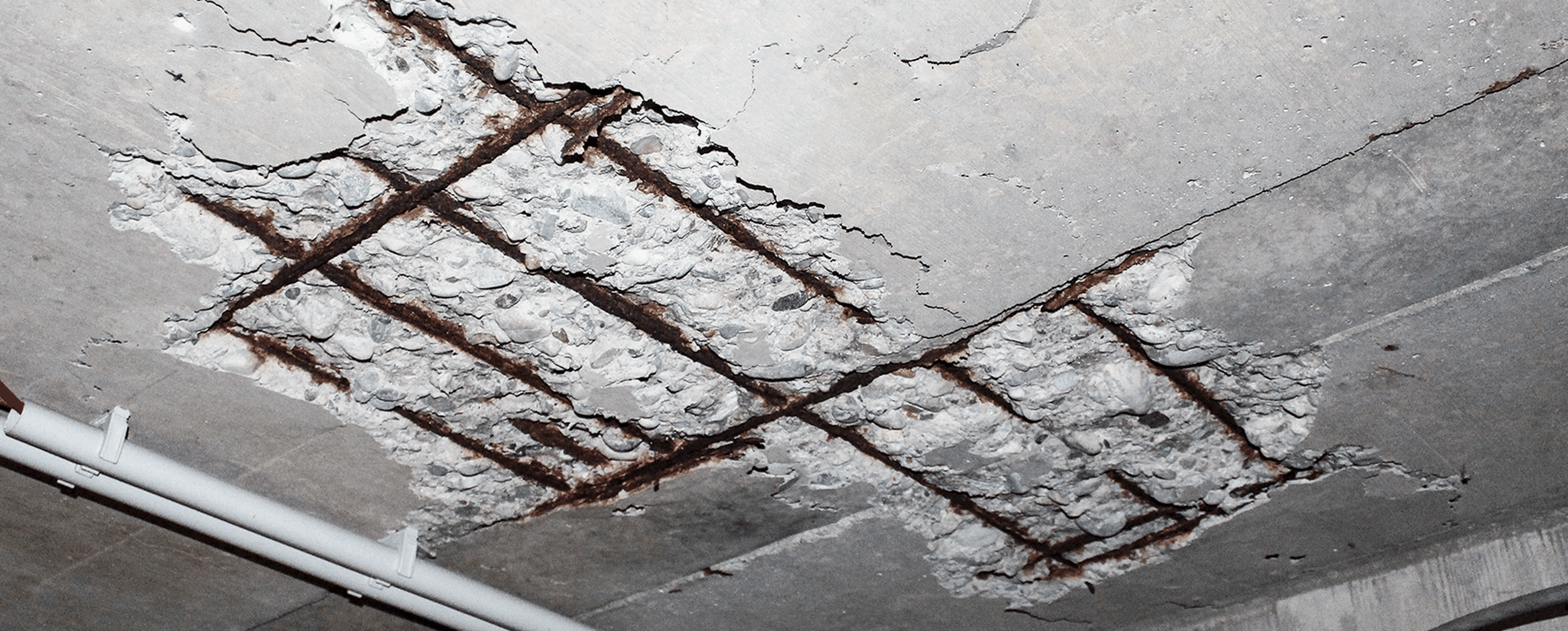 Beschädigte Betondecke mit freiliegenden rostigen Bewehrungsstäben, die Anzeichen von Verfall und strukturellen Problemen aufweisen.