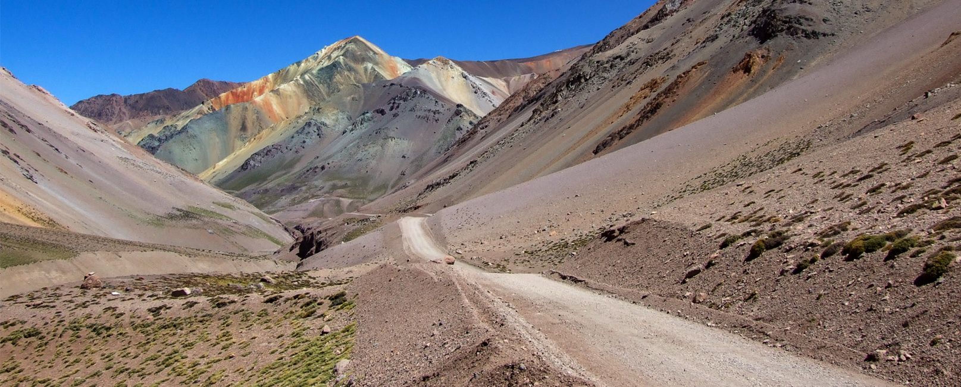Eine faszinierende Berglandschaft mit farbenfrohen Felsen und einer kurvigen Schotterstraße in einer trockenen Umgebung.