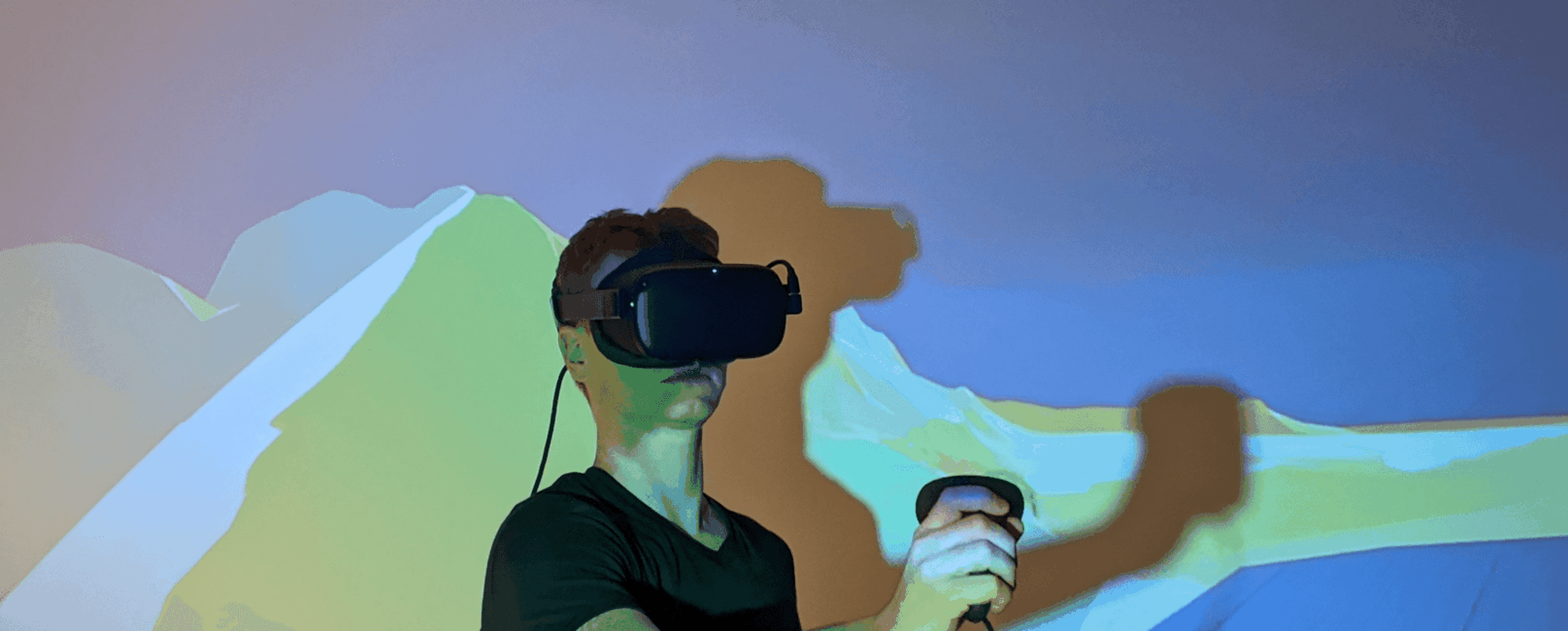 Eine Person mit einem VR-Headset und Controllern, mit bunten Projektionen an der Wand hinter ihr.