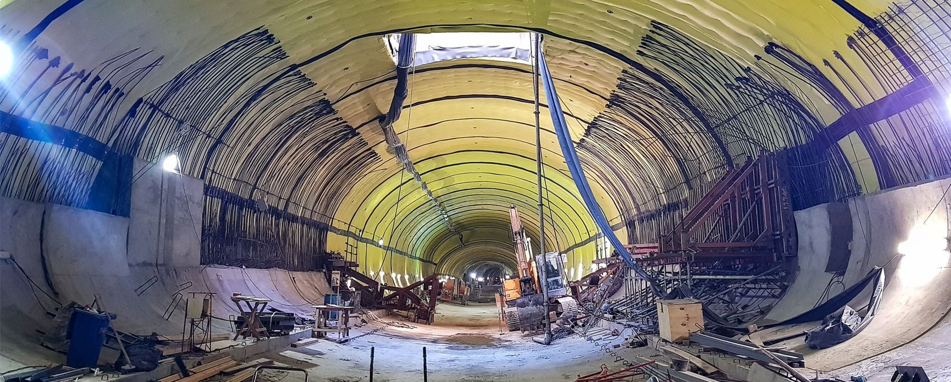 Eine Baustelle in einem Tunnel mit gelb gestrichener Decke und verschiedenen Baugeräten und -materialien.