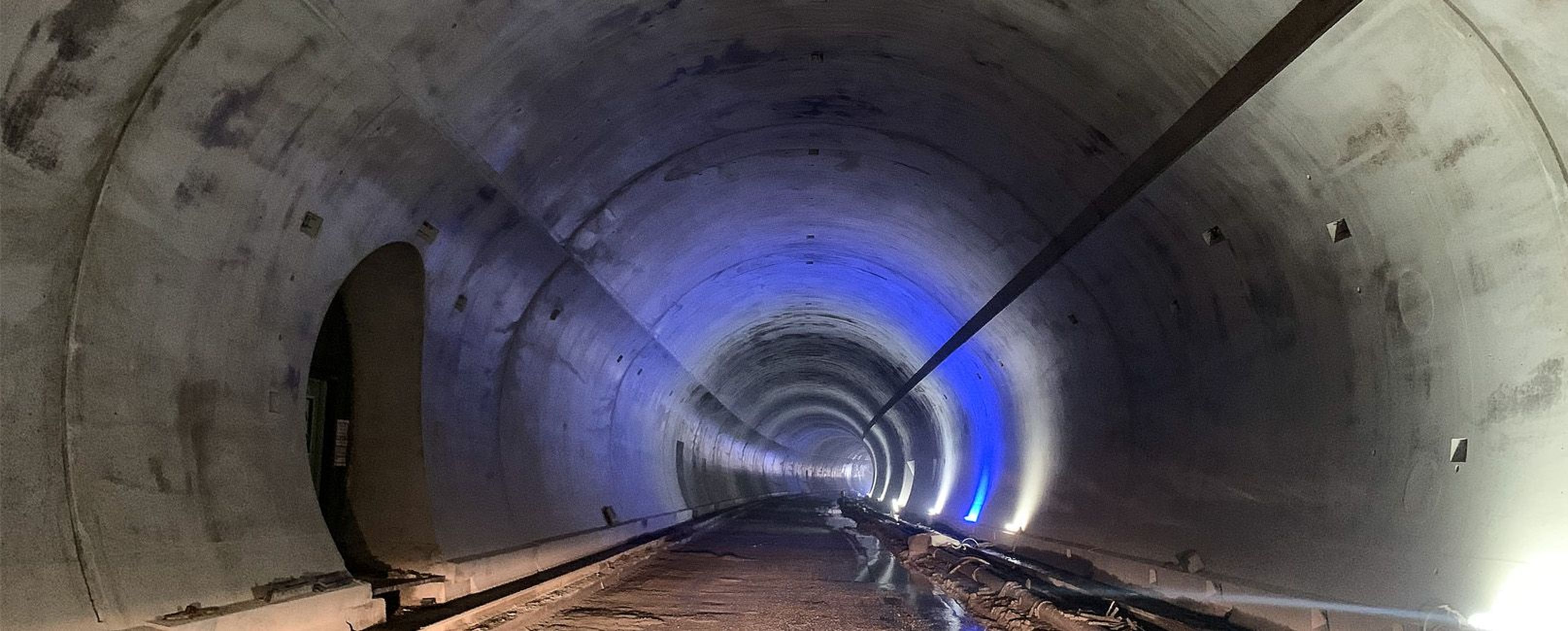 Ein langer, beleuchteter Tunnel mit geraden Wänden und Schienen am Boden, der in die Dunkelheit führt.