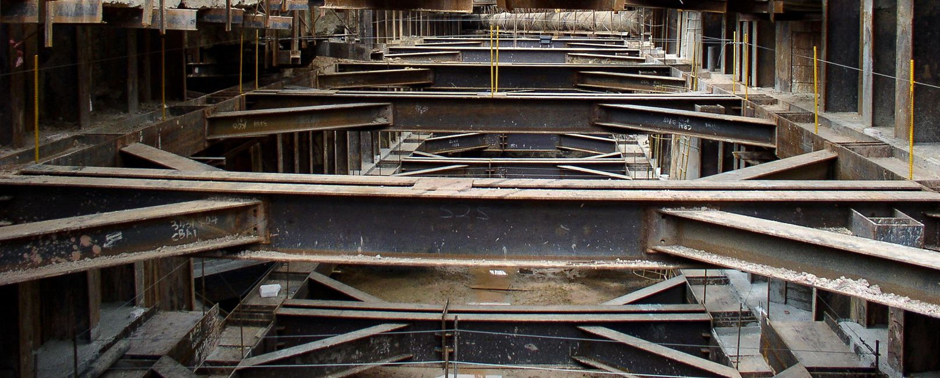 Innenansicht eines im Bau befindlichen Gebäudes mit freiliegenden Stahlträgern und einer teilweise fertiggestellten Struktur.