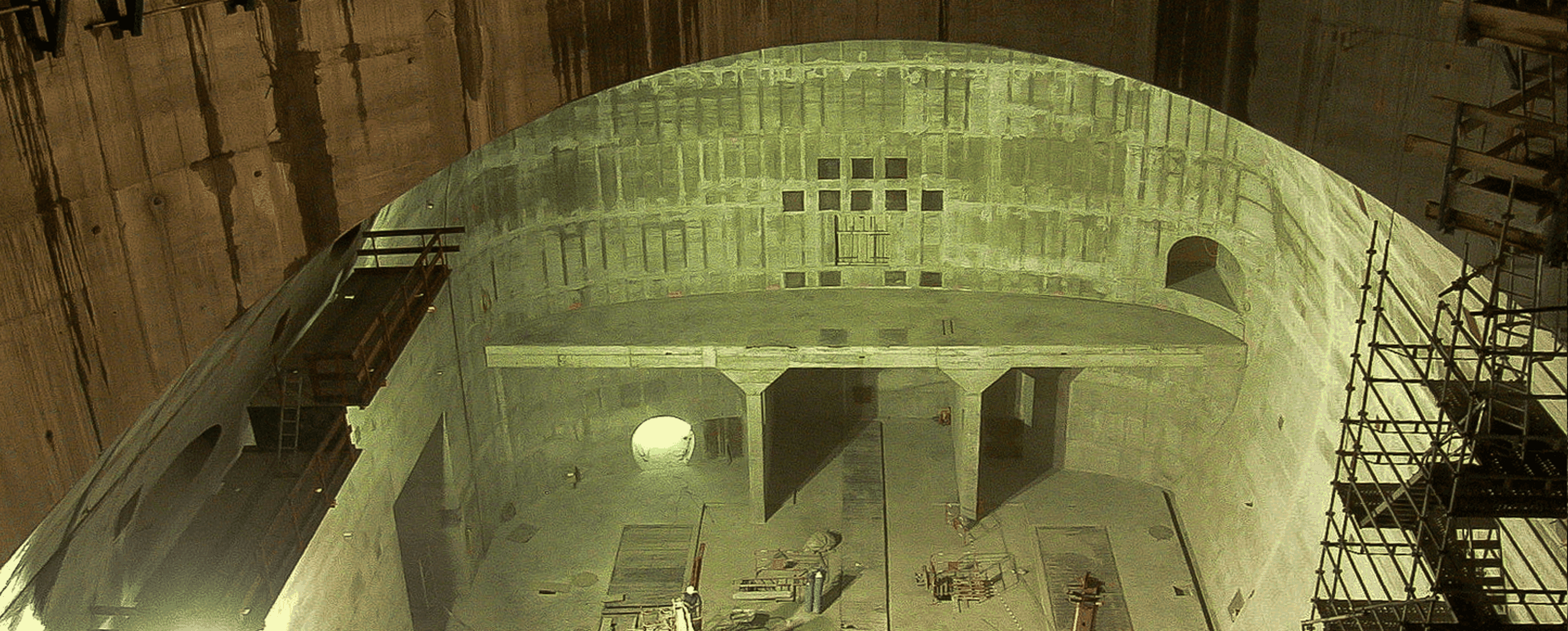 Eine große, unvollendete, betonierte Baugrube mit einem geschwungenen Dach und Baugerüsten im Hintergrund.