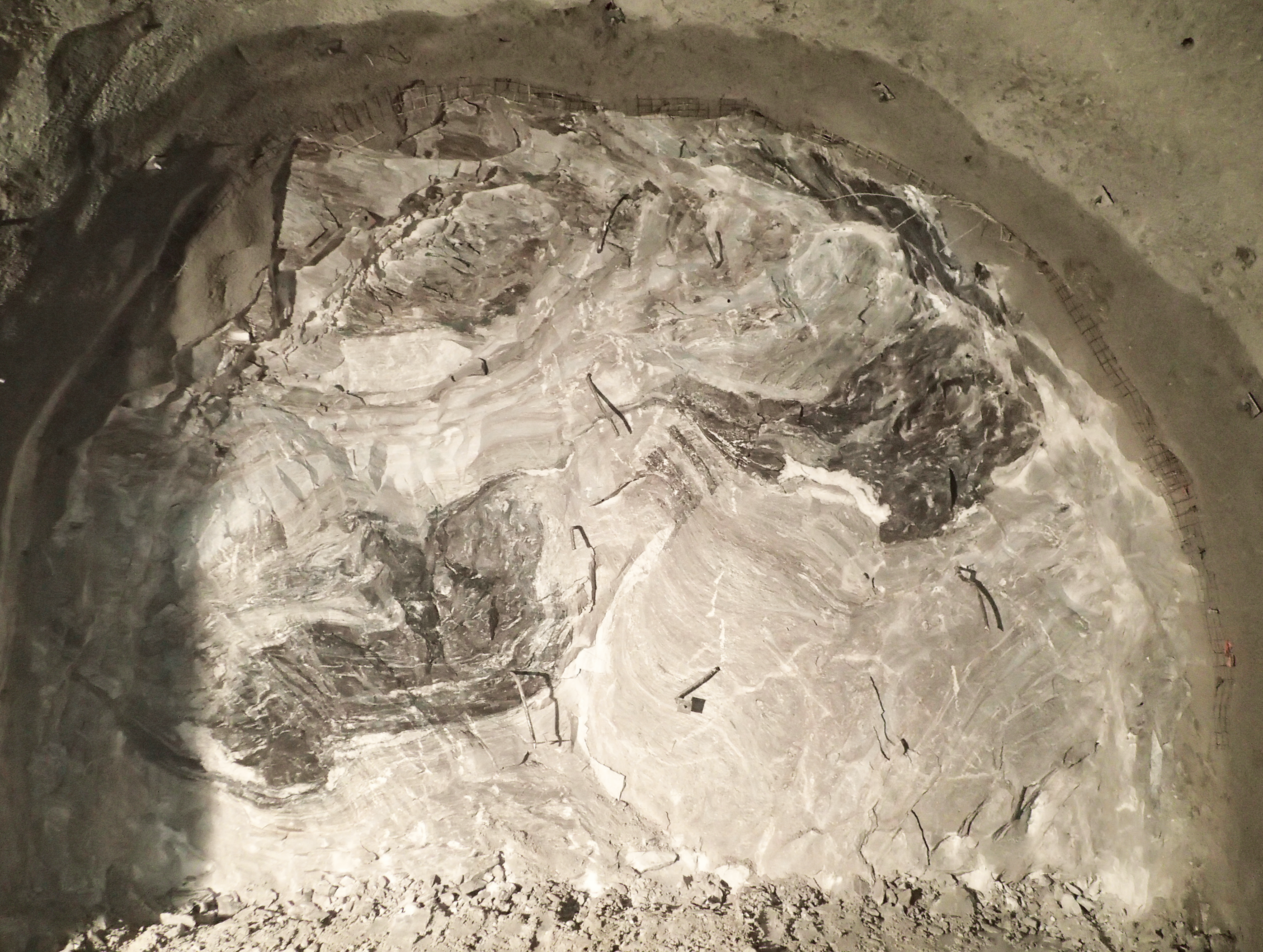 Luftaufnahme einer großen, felsigen Ausgrabungsstätte mit freigelegten Erd- und Gesteinsschichten, die unterschiedliche Texturen und Grau- und Brauntöne aufweisen.