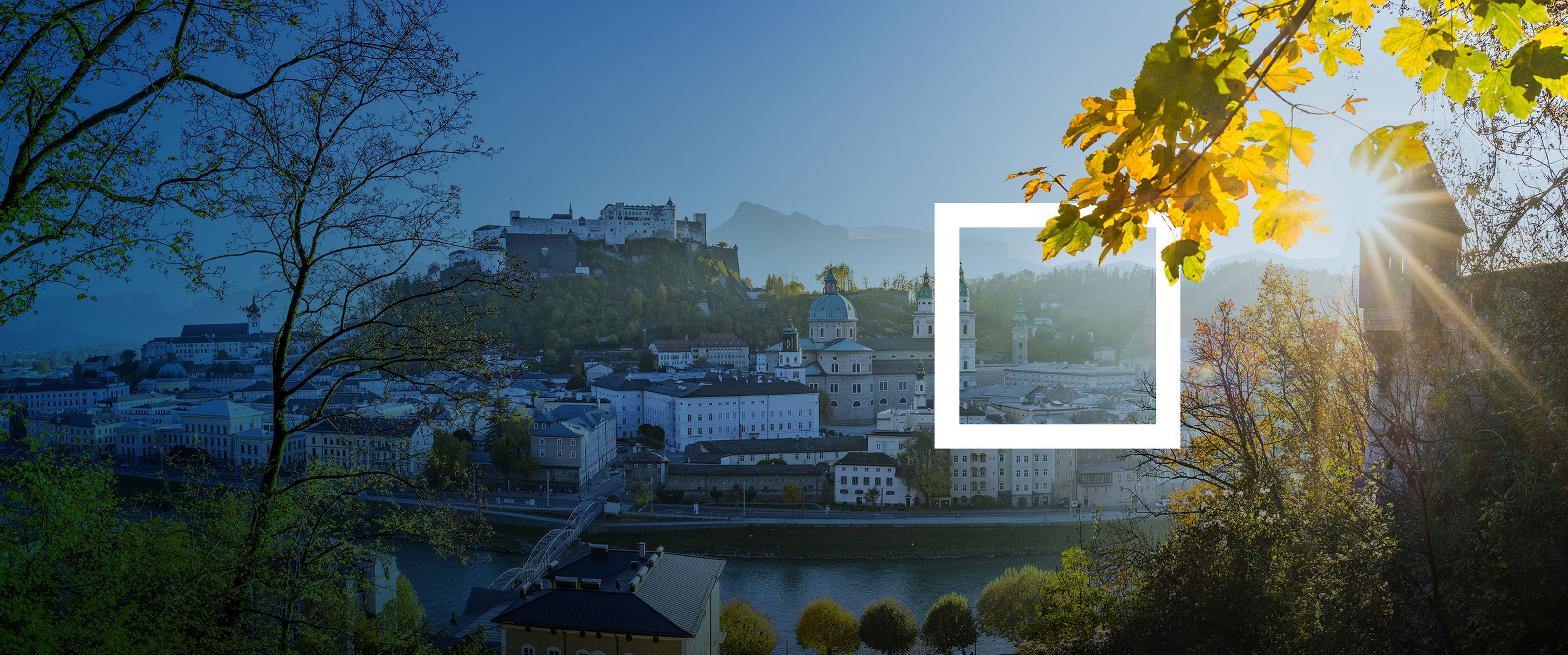 Eine Landschaft mit einer Stadtansicht, einem Fluss und Bäumen im Vordergrund, beleuchtet von der Sonne.