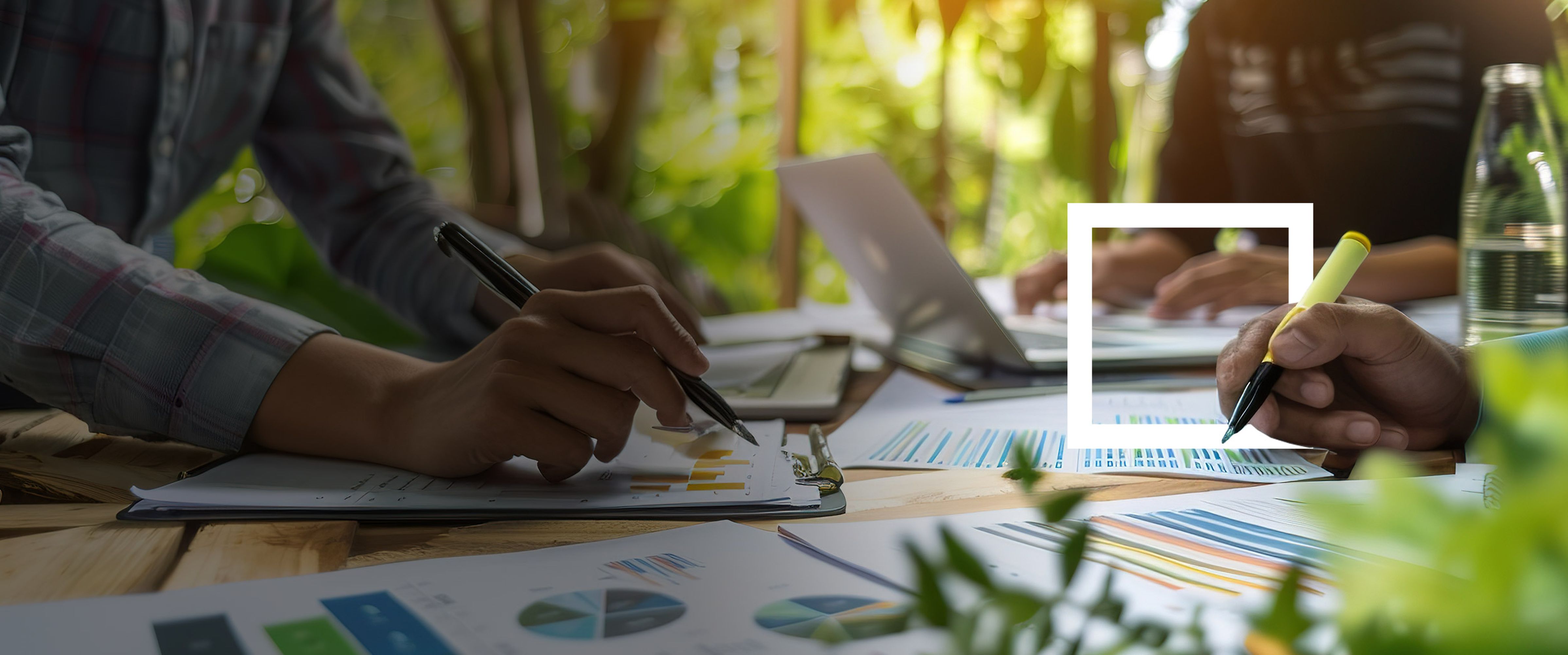 Several hands work at a table with documents and diagrams in a green environment.