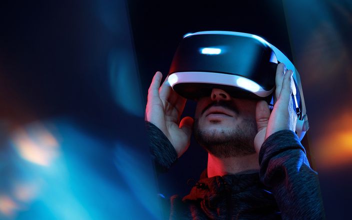 Eine Person trägt ein VR-Headset in einem dunklen Raum mit bunten Lichtern im Hintergrund.